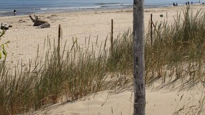 A beach scene with a wooden post and a blank sign, sandy dunes, and the ocean in the background. - Villa Zosieńka (Gdansk)