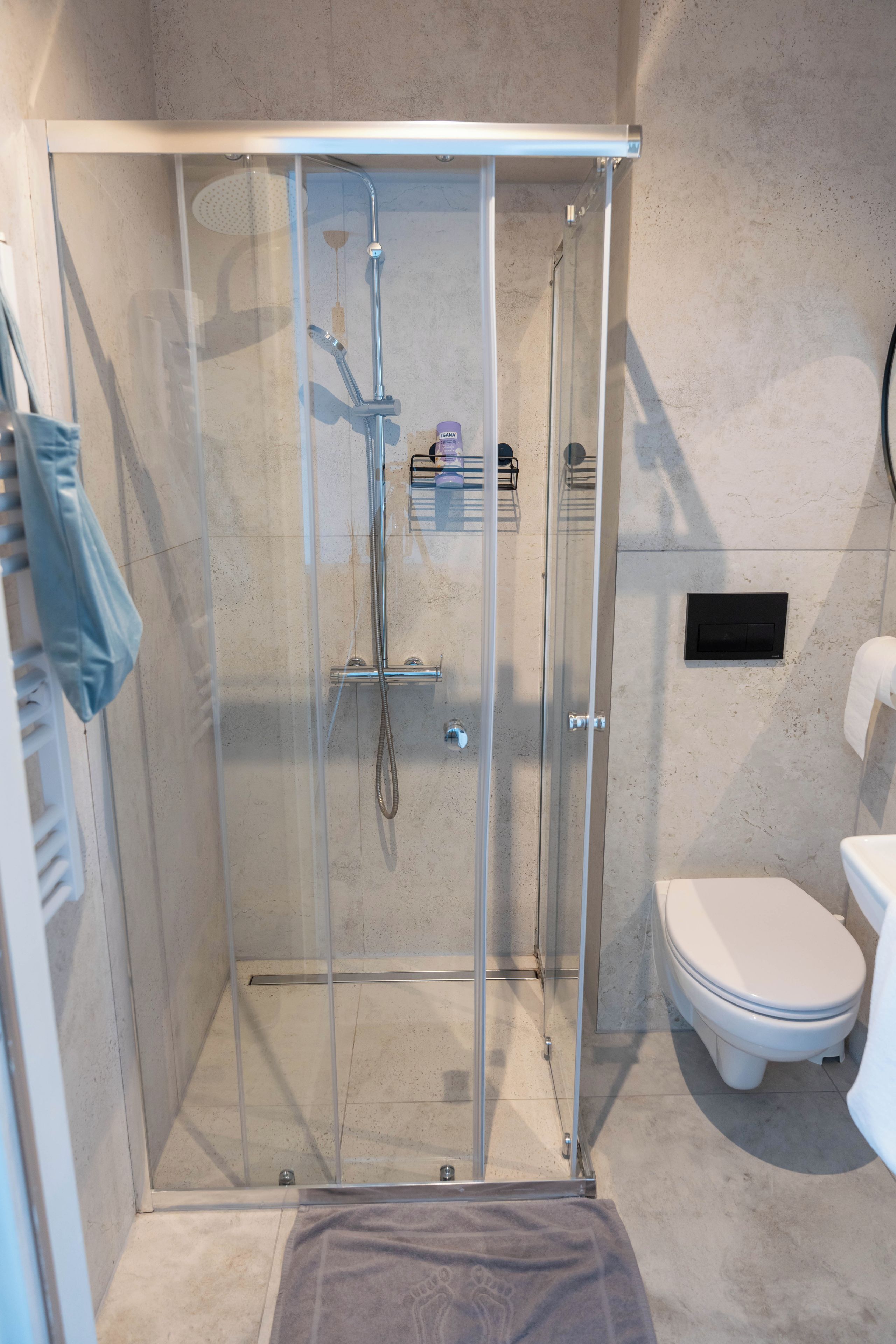 A glass-enclosed shower with a handheld showerhead and a wall-mounted faucet.
