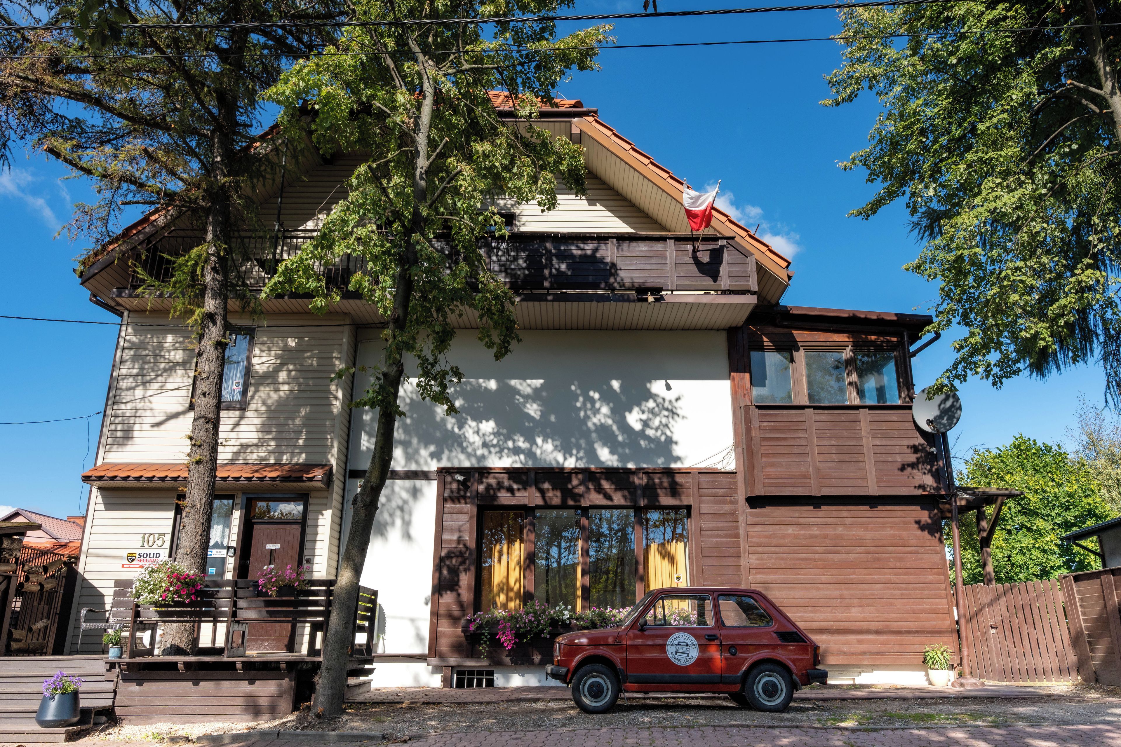 A two-story building with a balcony, a car parked in front, and a flag on the roof.
