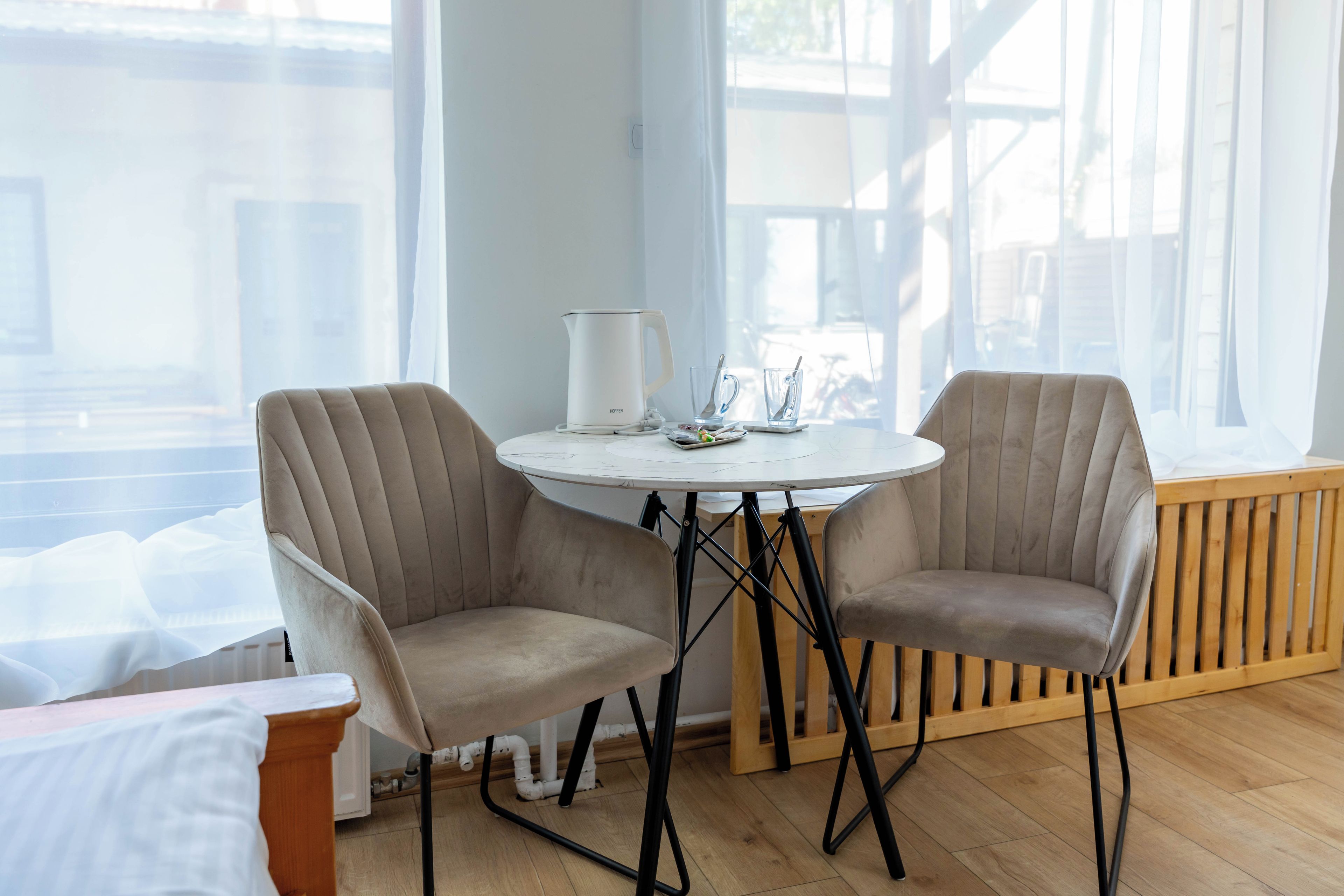 Una habitación con una mesa redonda, dos sillas, un hervidor blanco y un ventanal con vistas al exterior.