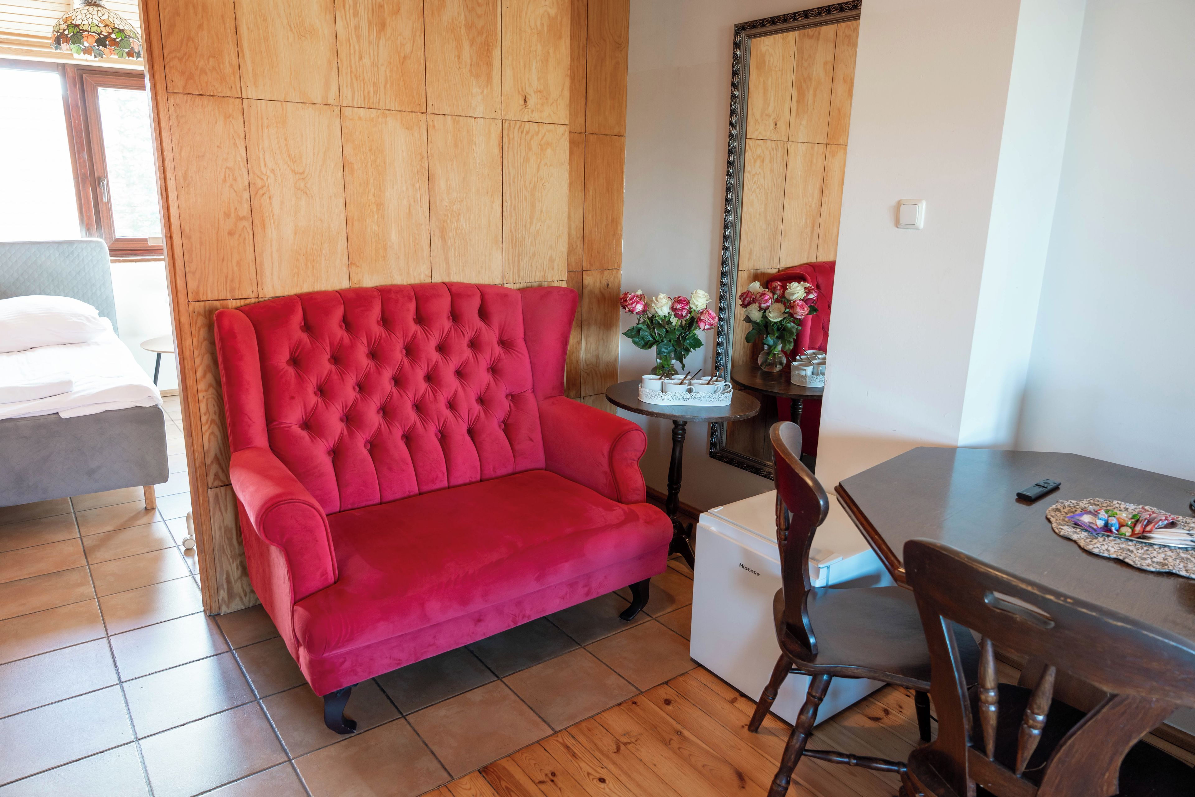 Un sofá rojo, una mesa de comedor y un espejo en una habitación con paneles de madera y suelo de baldosas.