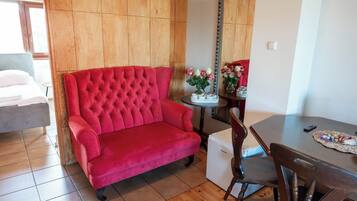 Un sofá rojo, una mesa de comedor y un espejo en una habitación con paneles de madera y suelo de baldosas.