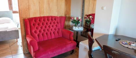 A red sofa, a dining table, and a mirror in a room with wooden paneling and tiled flooring.