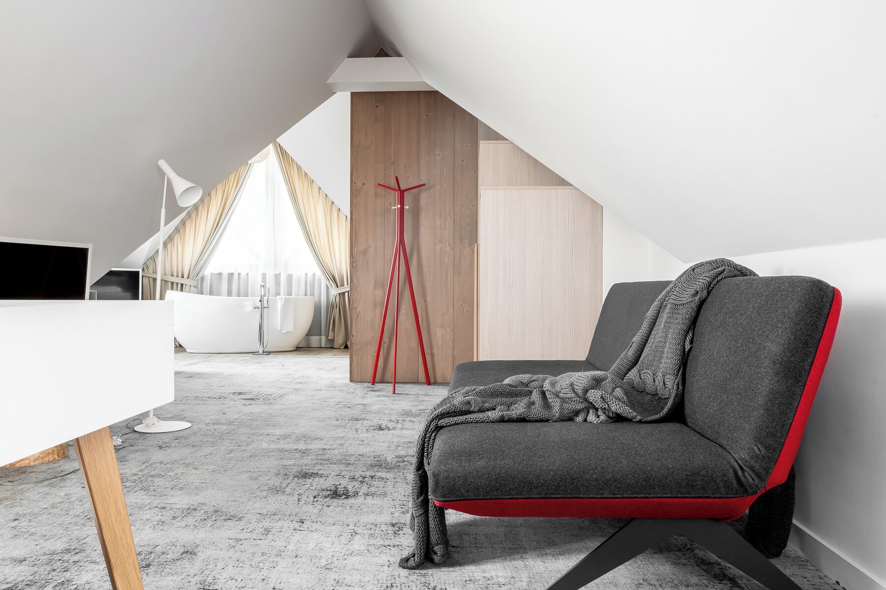 Ein modernes Schlafzimmer im Loft-Stil mit grauem Sofa, weißem Schreibtisch, roter Stehlampe und einem Holzschrank.
