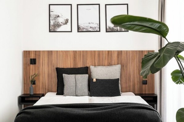 A bedroom with a wooden headboard, a bed with white and grey bedding, and three framed pictures on the wall.