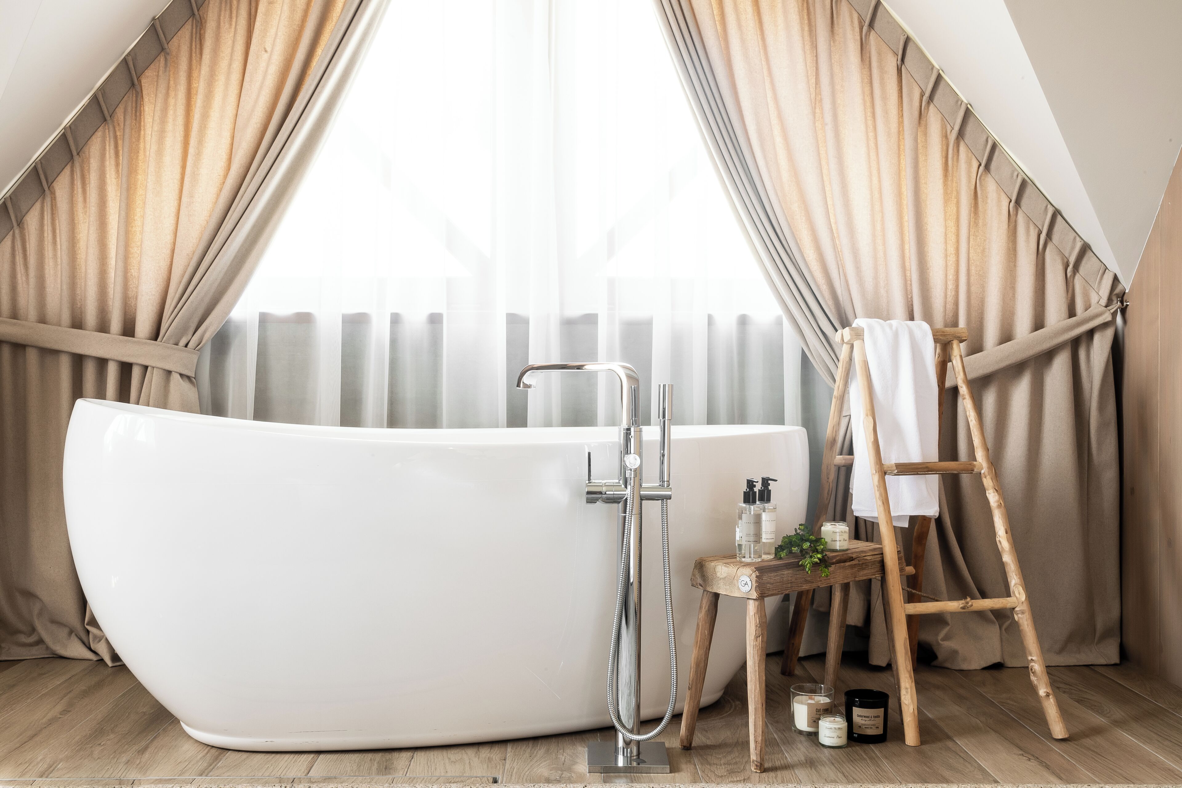 A modern bathroom with a freestanding bathtub, a showerhead, and a wooden stool with toiletries.
