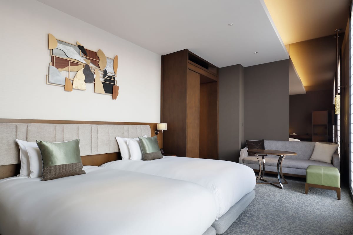 Quarto de hotel com uma cama grande, um sofá, uma mesinha e uma obra de arte abstrata na parede.
