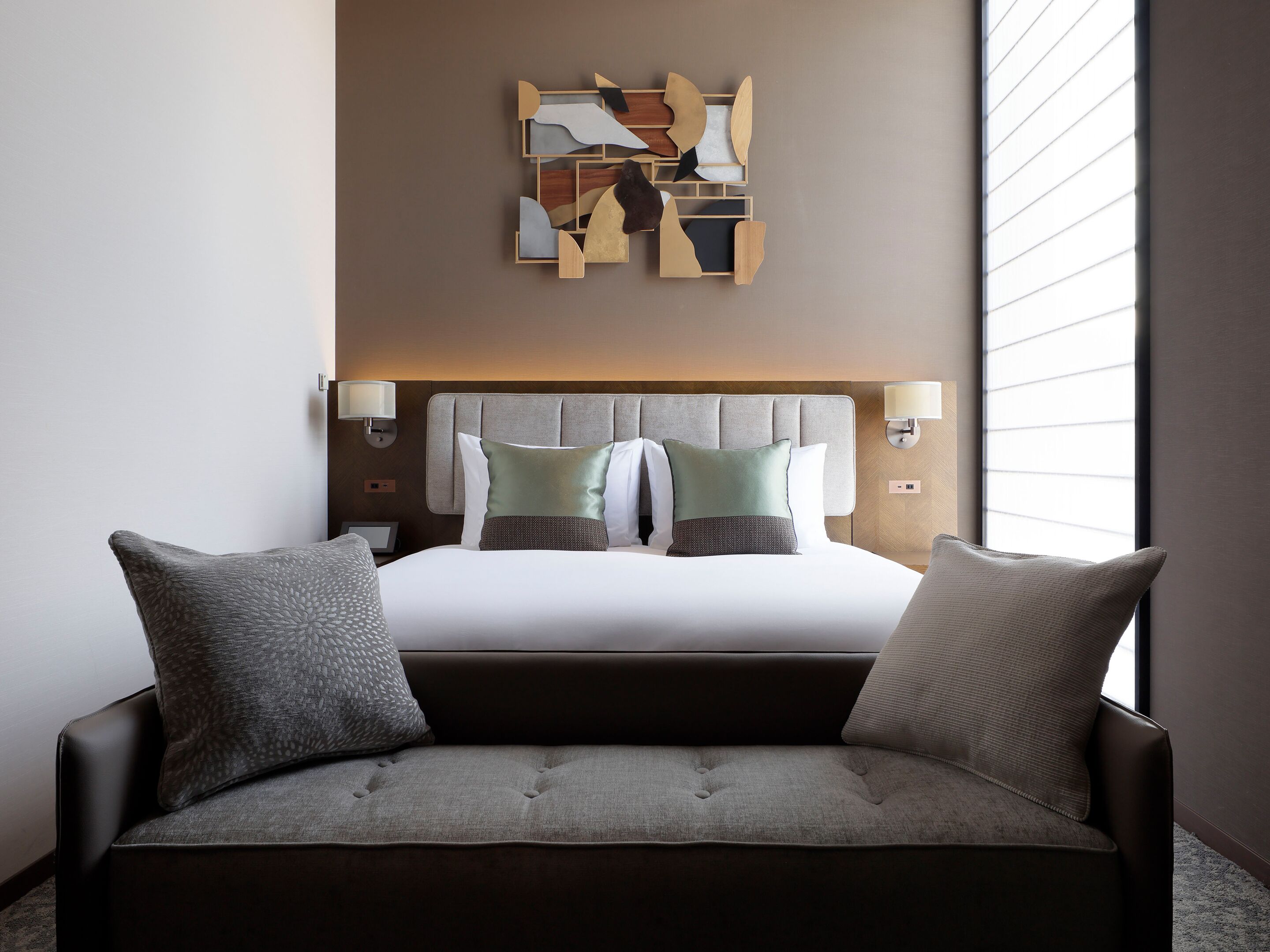 Une chambre d’hôtel avec un lit, deux lampes de chevet, une œuvre d’art murale et un canapé.