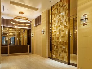 A modern elevator interior with a geometric patterned wall, a circular light fixture, and a mirrored wall.