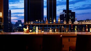 Un bar con vistas a un horizonte urbano, botellas, vasos y una barra de madera.
