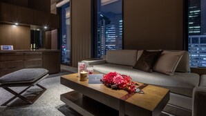 Una sala de estar moderna con un sofá, una mesa de centro con flores, una silla y vistas de la ciudad de noche.