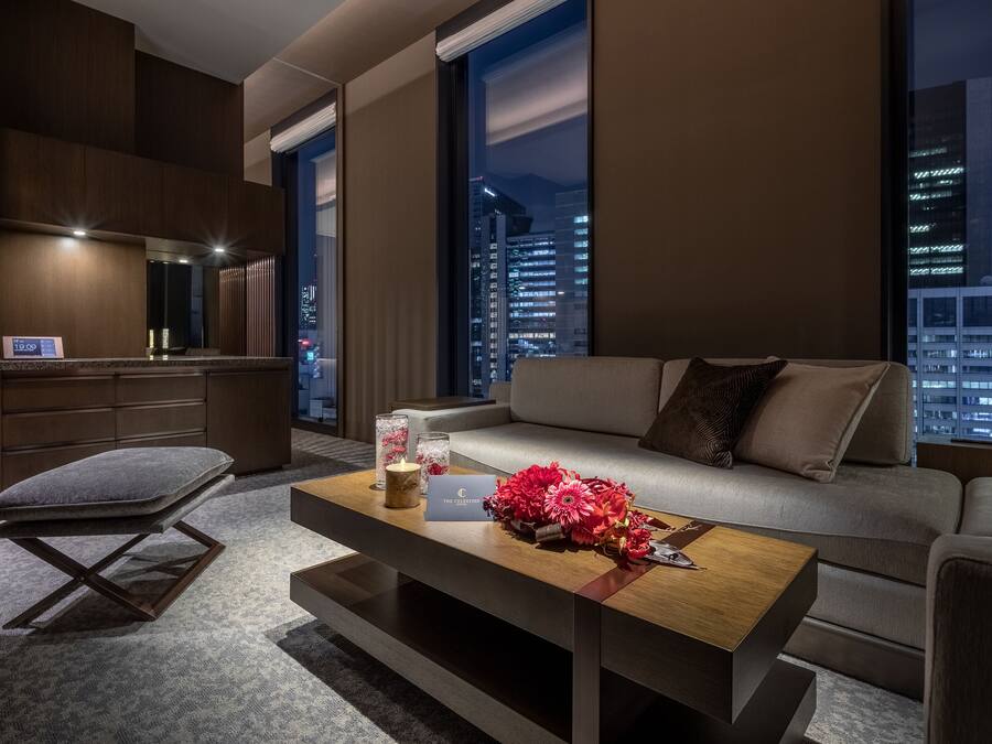 Una sala de estar moderna con un sofá, una mesa de centro con flores, una silla y vistas de la ciudad de noche.