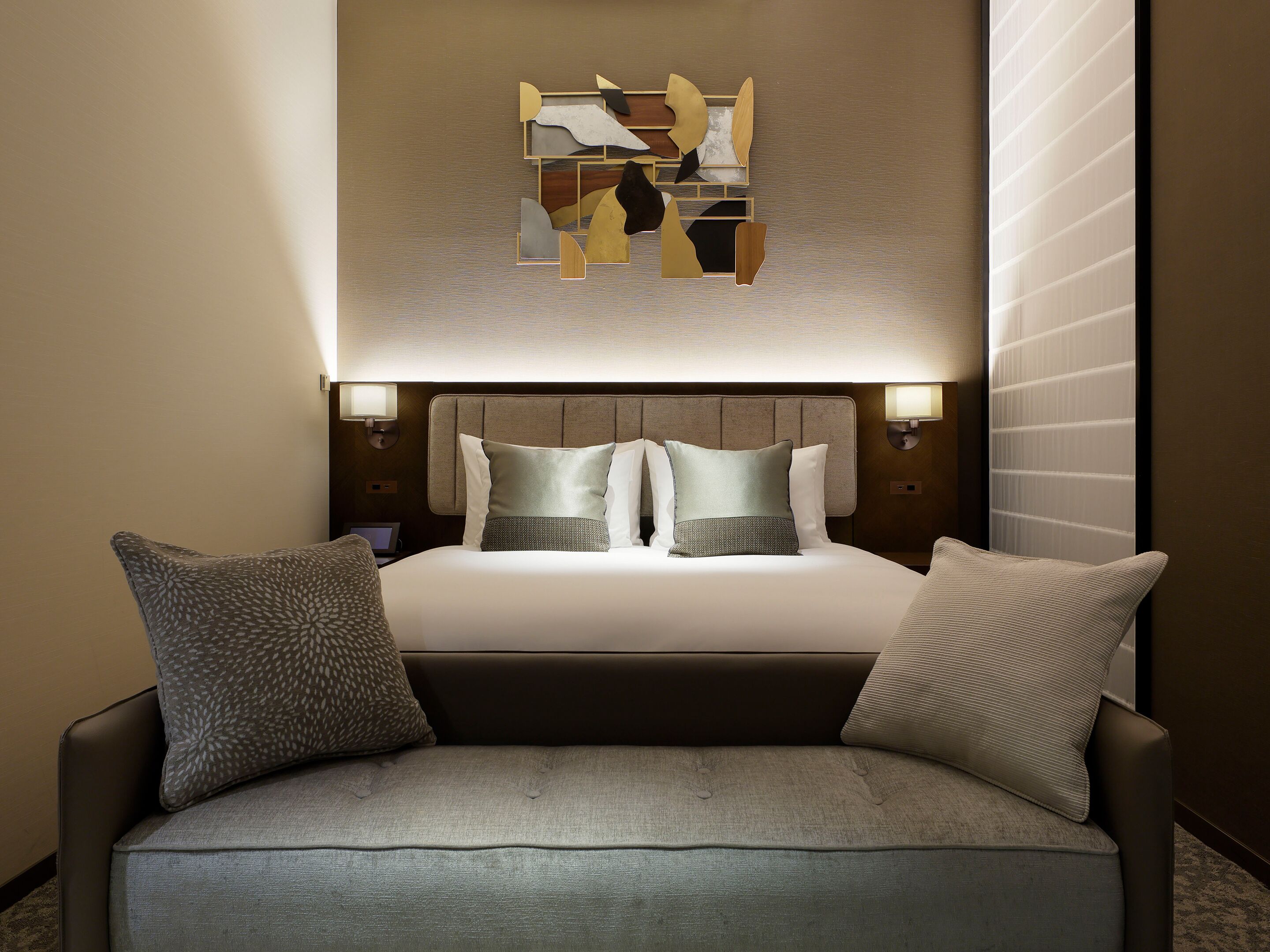 Une chambre d’hôtel avec un lit, deux lampes de chevet, une œuvre d’art murale et un canapé.