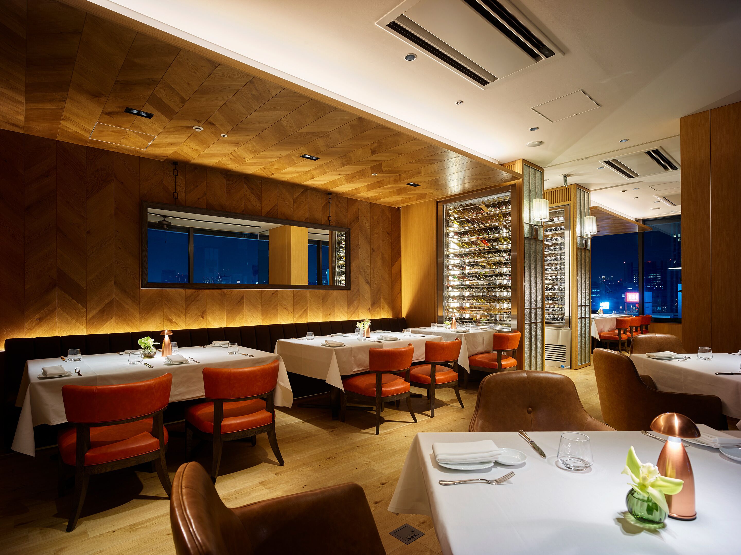 A restaurant with wooden panel walls, multiple tables with white tablecloths, and red chairs.