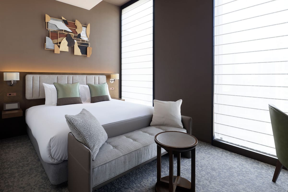 Quarto de hotel moderno com uma cama grande, um sofá, uma mesa pequena e uma obra de arte na parede.