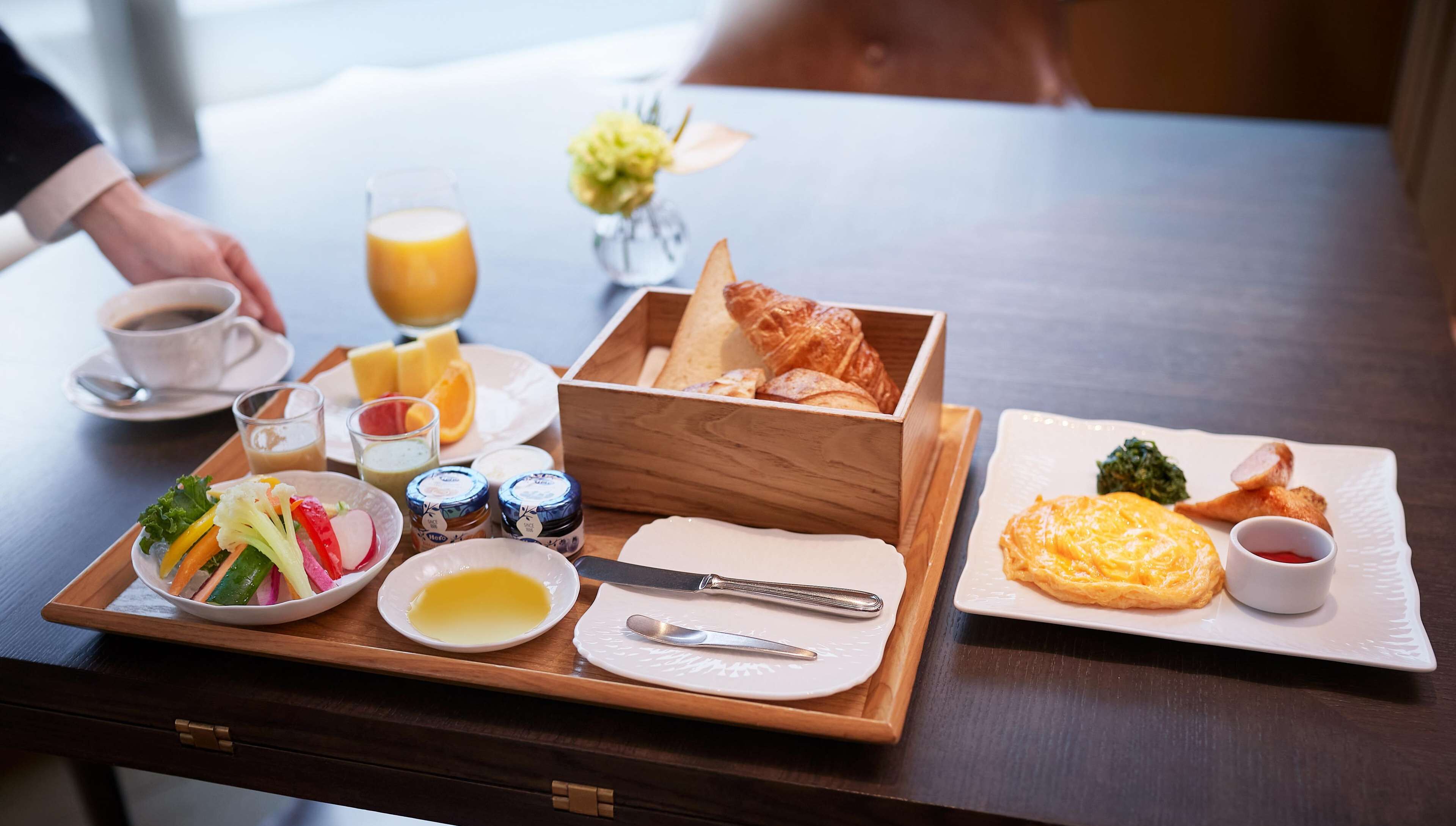 A breakfast tray with croissants, omelette, salad, and beverages on a wooden table.