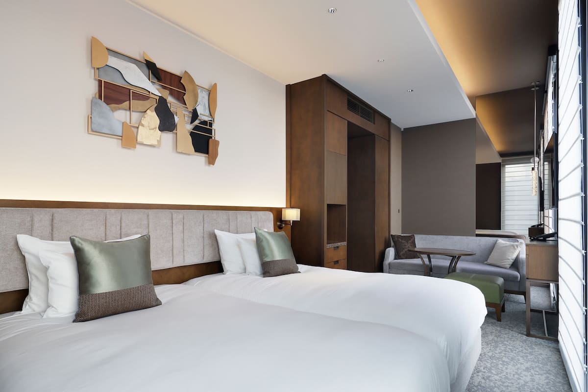 Quarto de hotel com uma cama grande, uma mesa, uma cadeira e vista para o exterior.
