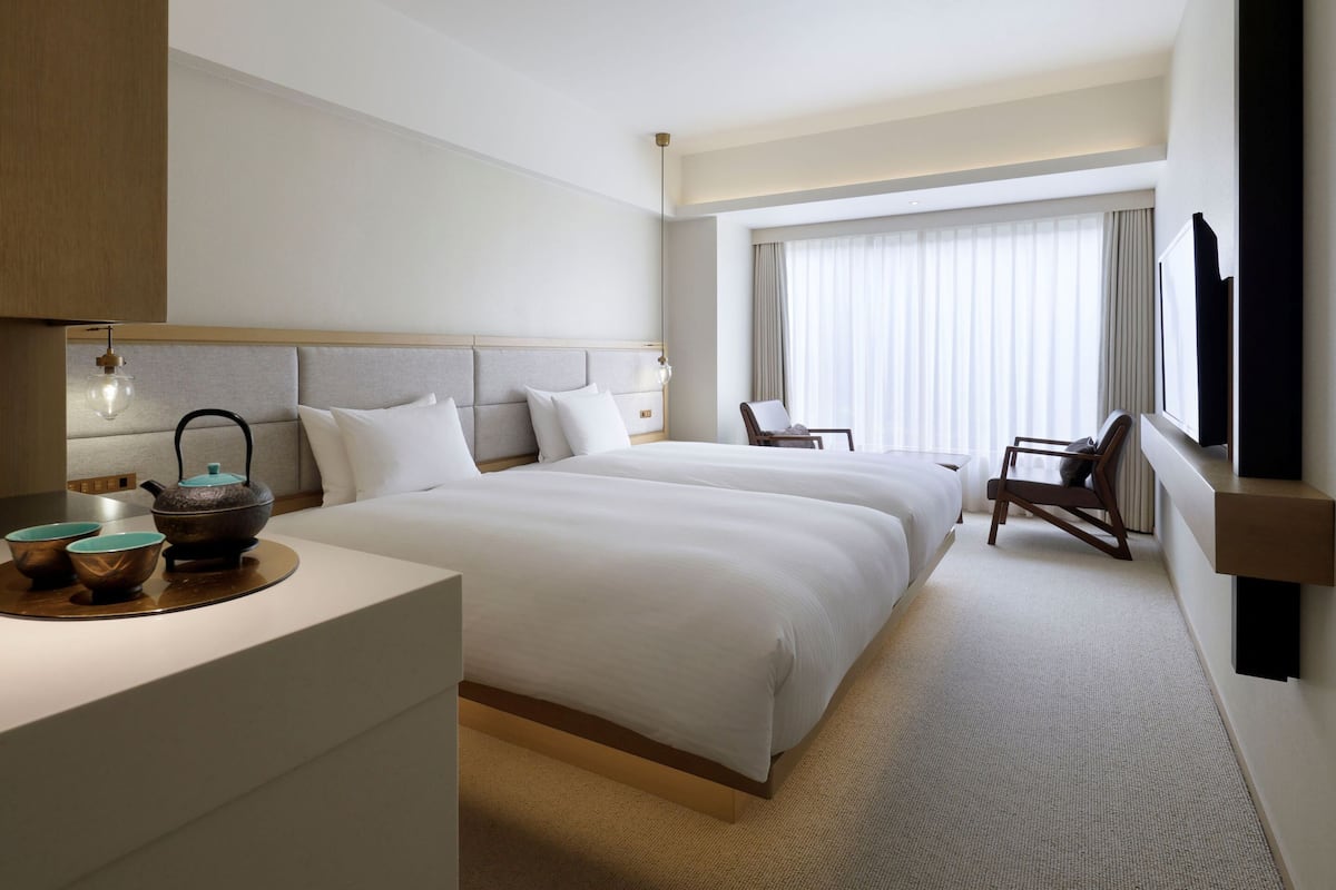 A hotel room with a large bed, a desk with a kettle, a chair, and a TV mounted on the wall.