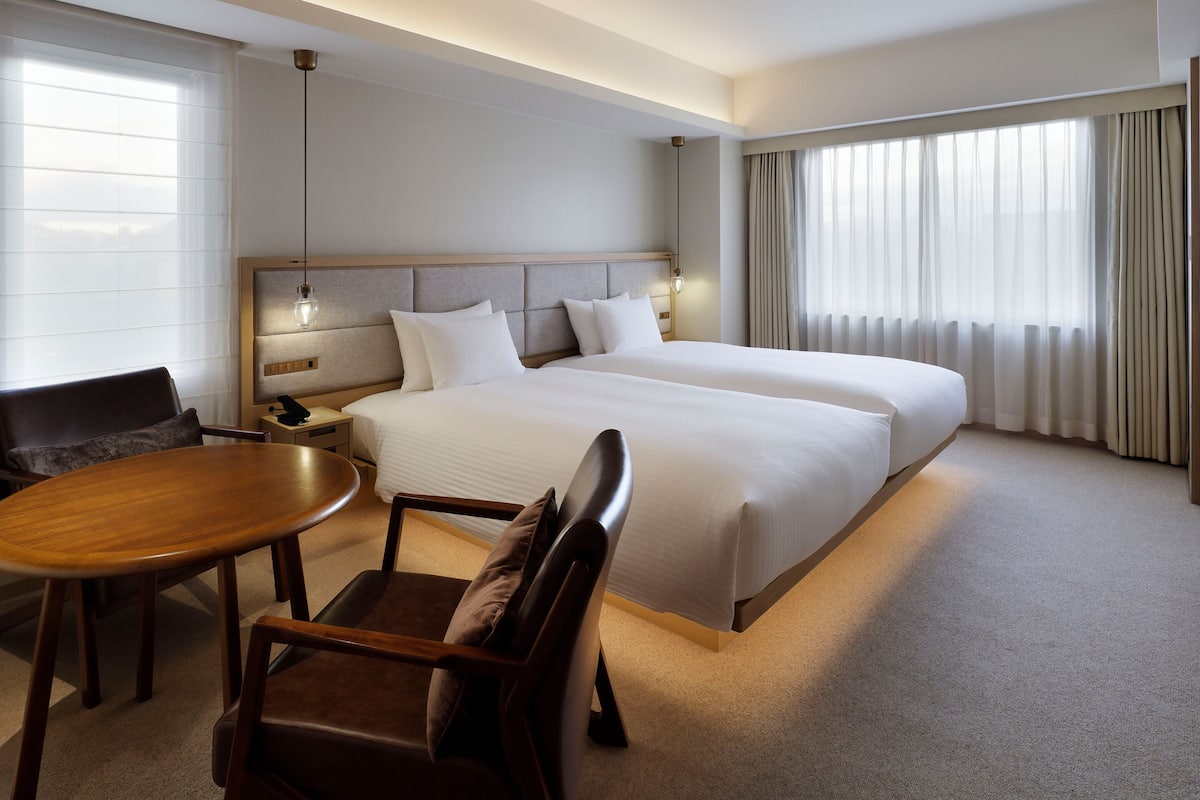 A hotel room with a large bed, a desk, a chair, and a window with curtains.