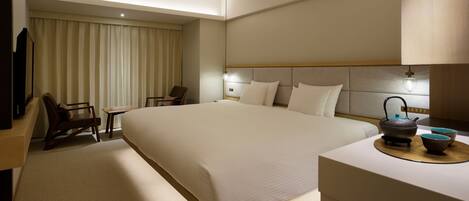 A hotel room with a large bed, a desk, a chair, a television, and a tea set.