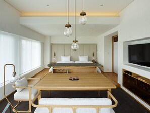 A modern bedroom with a large bed, bedside tables, a TV, and a dining area with a wooden table and chairs.
