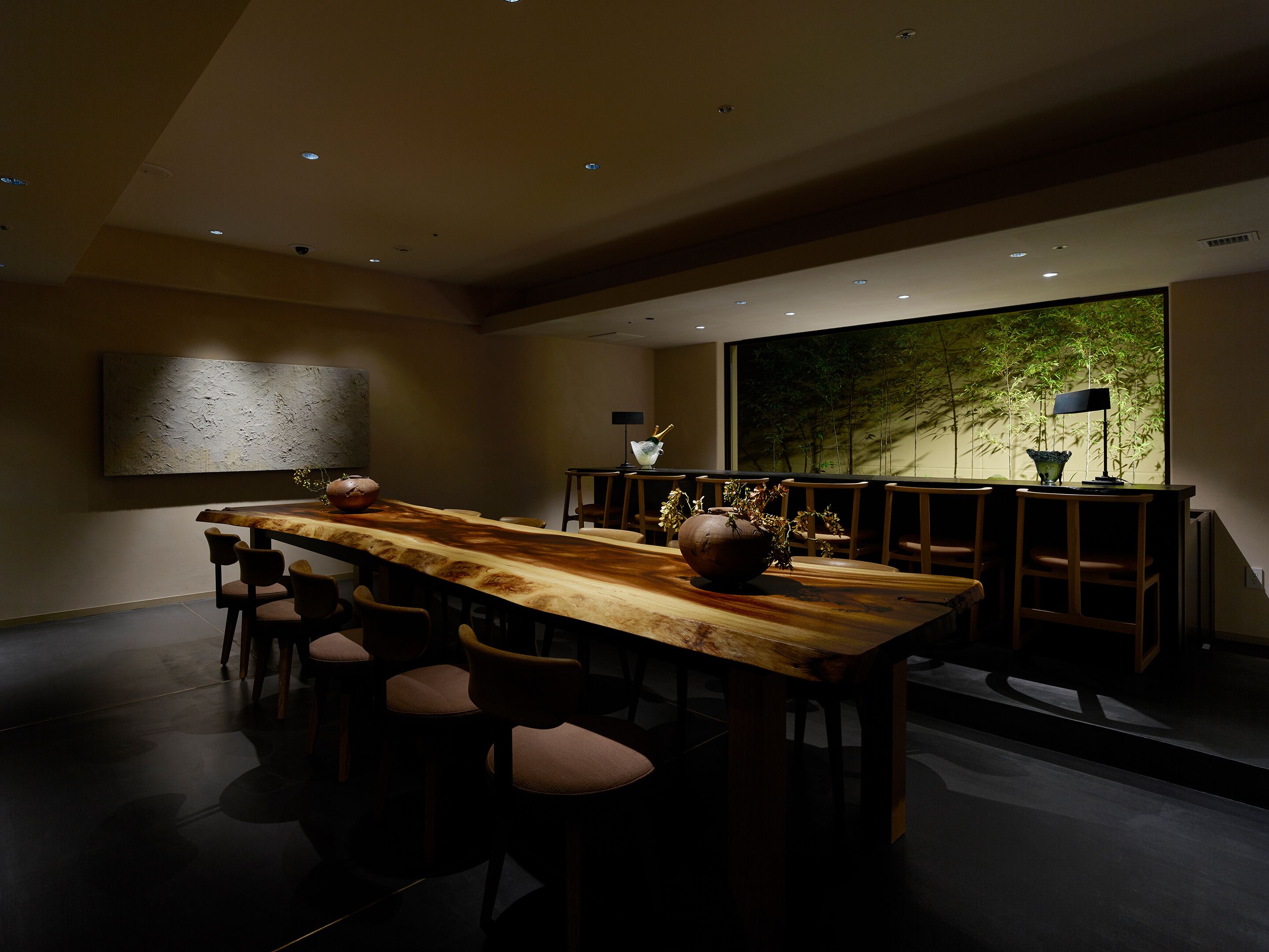Un espace repas moderne avec une longue table en bois, plusieurs chaises et une grande fenêtre donnant sur un paysage verdoyant.