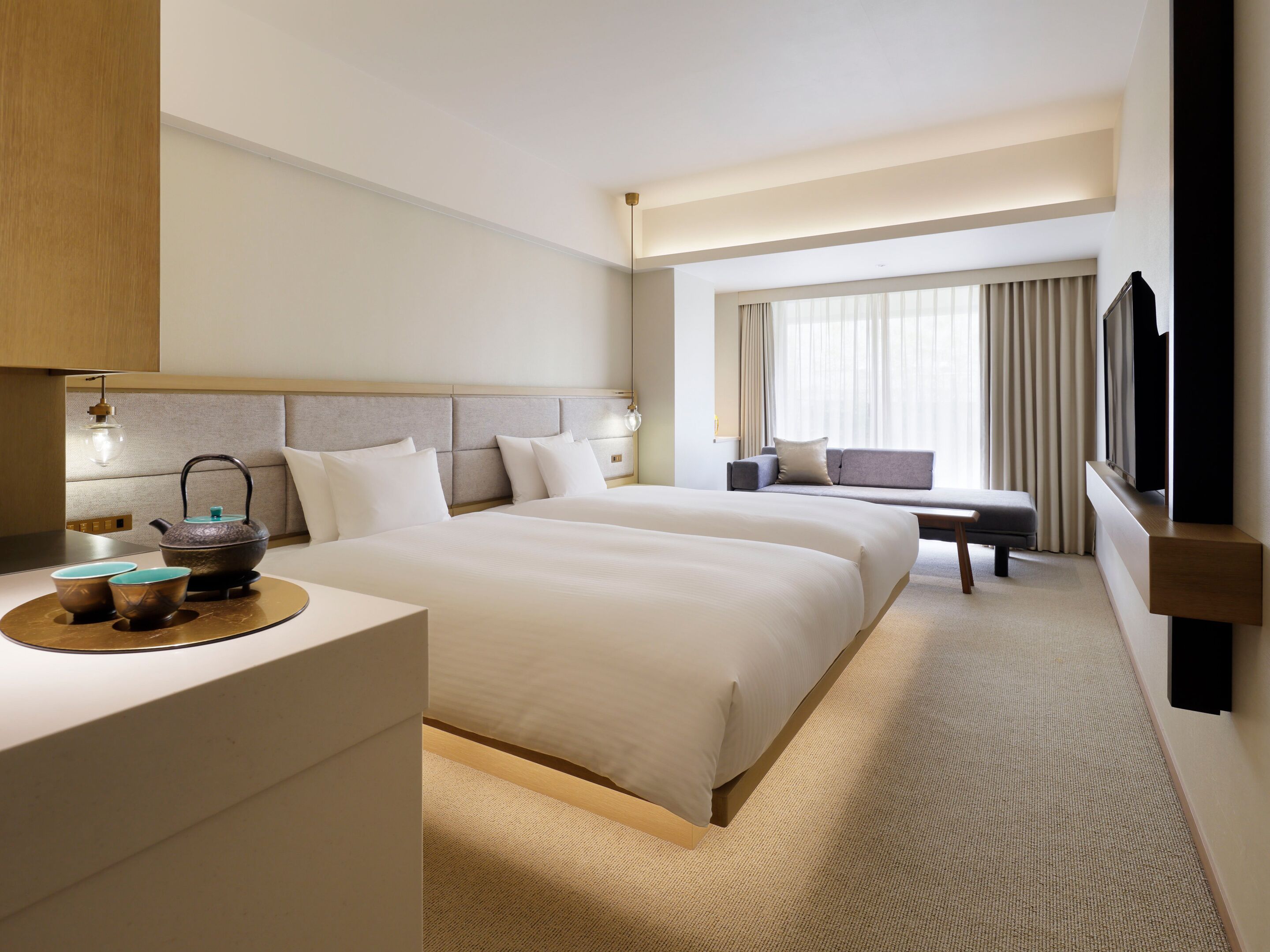 A hotel room with two beds, a desk with a kettle, and a TV.