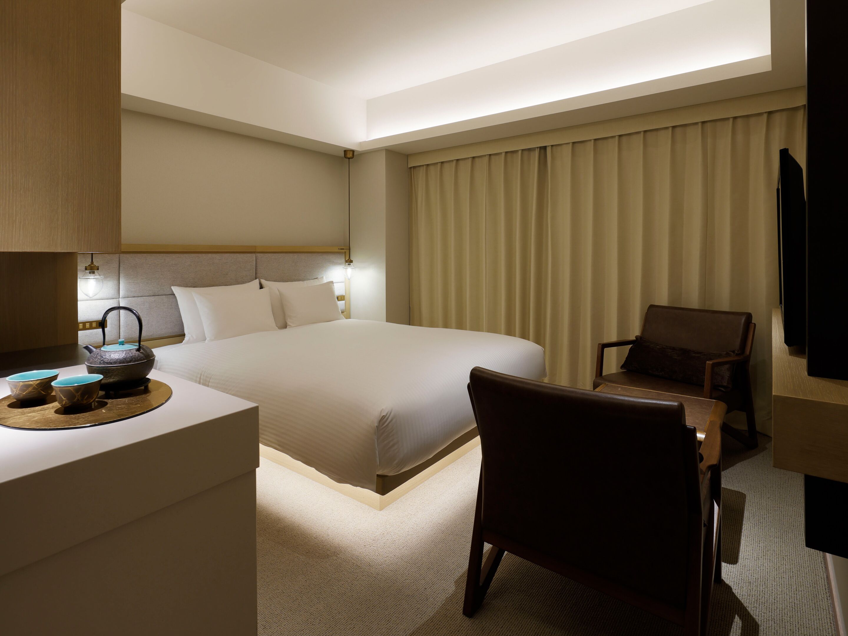 Una habitación de hotel con una cama, un escritorio con hervidor, una silla y un televisor.