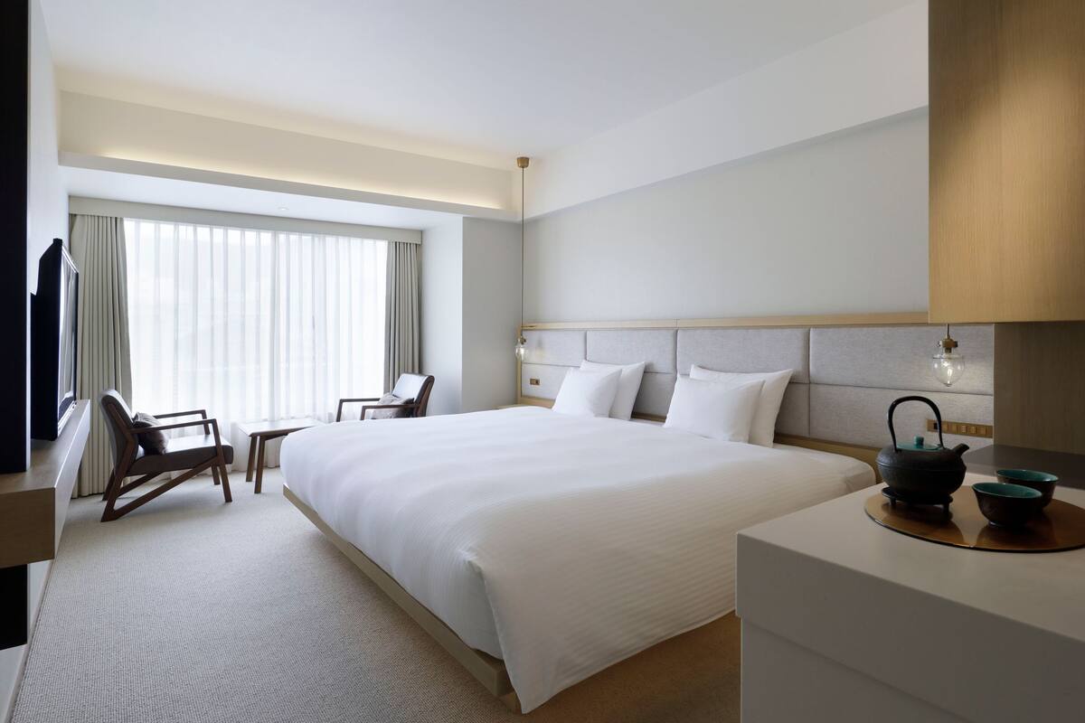 A hotel room with a large bed, a desk, a chair, a TV, and a window with curtains.