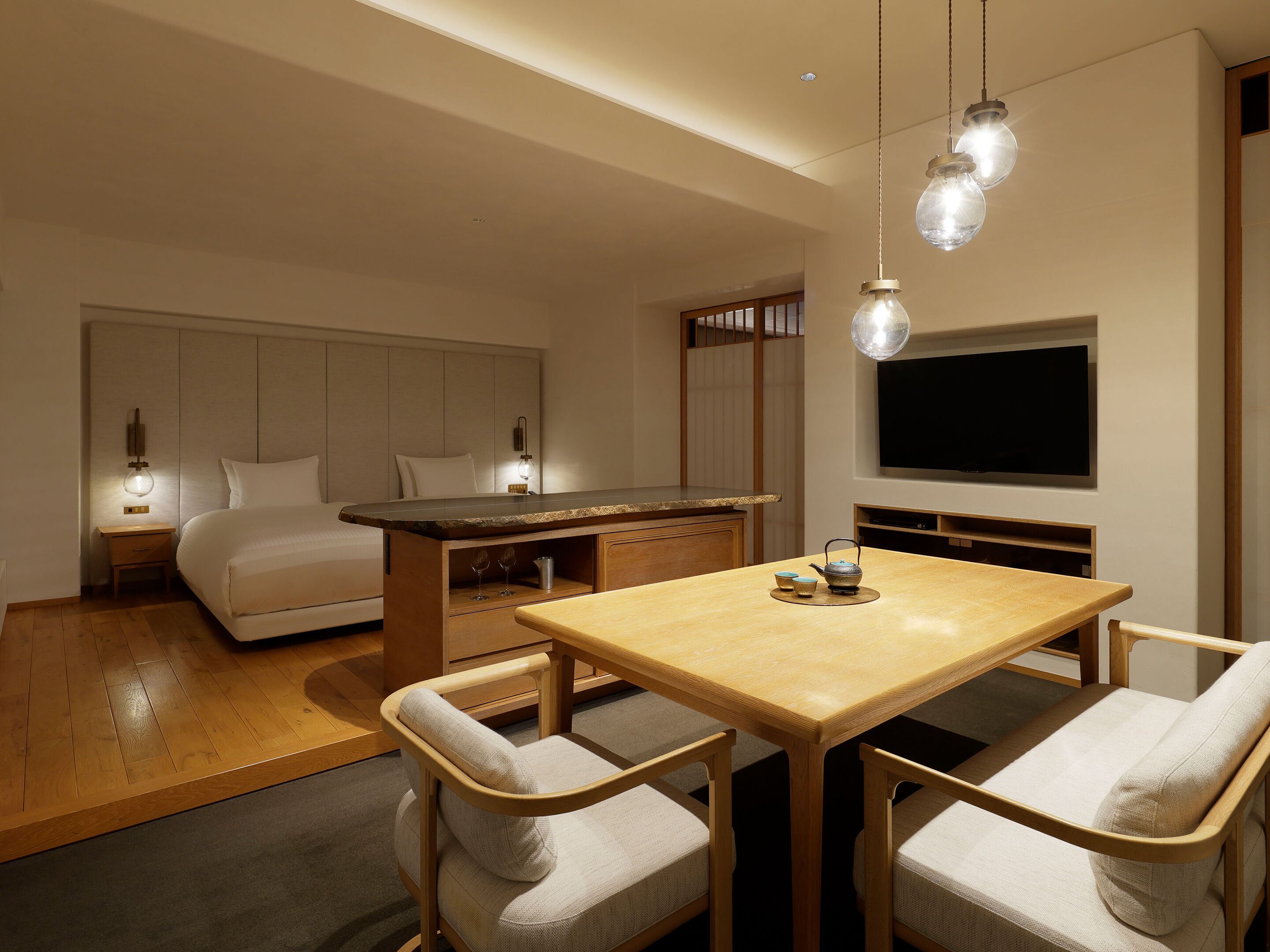 A hotel room with a bed, a desk, a TV, and a dining area with chairs.
