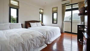 Habitación de hotel con dos camas, suelo de madera, ventanas amplias con cortinas y vistas al exterior.
