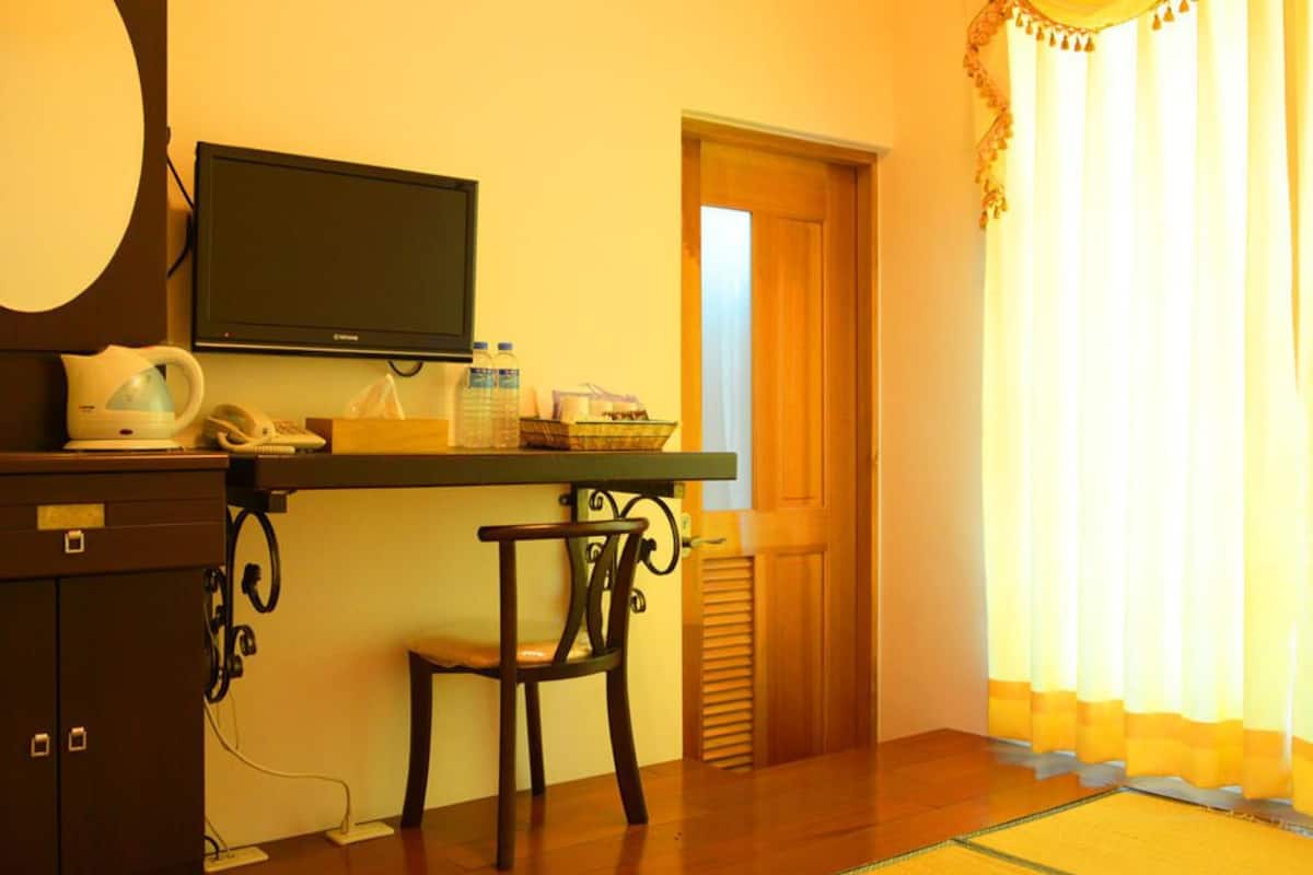 Quarto de hotel com escrivaninha, cadeira, televisão e porta que dá para outro aposento.