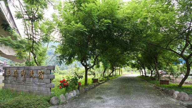 Un sendero bordeado de árboles y un cartel de piedra con caracteres chinos.