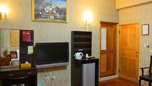 Habitación de hotel con televisor, refrigerador pequeño, escritorio con silla, puerta de madera y un cuadro en la pared.