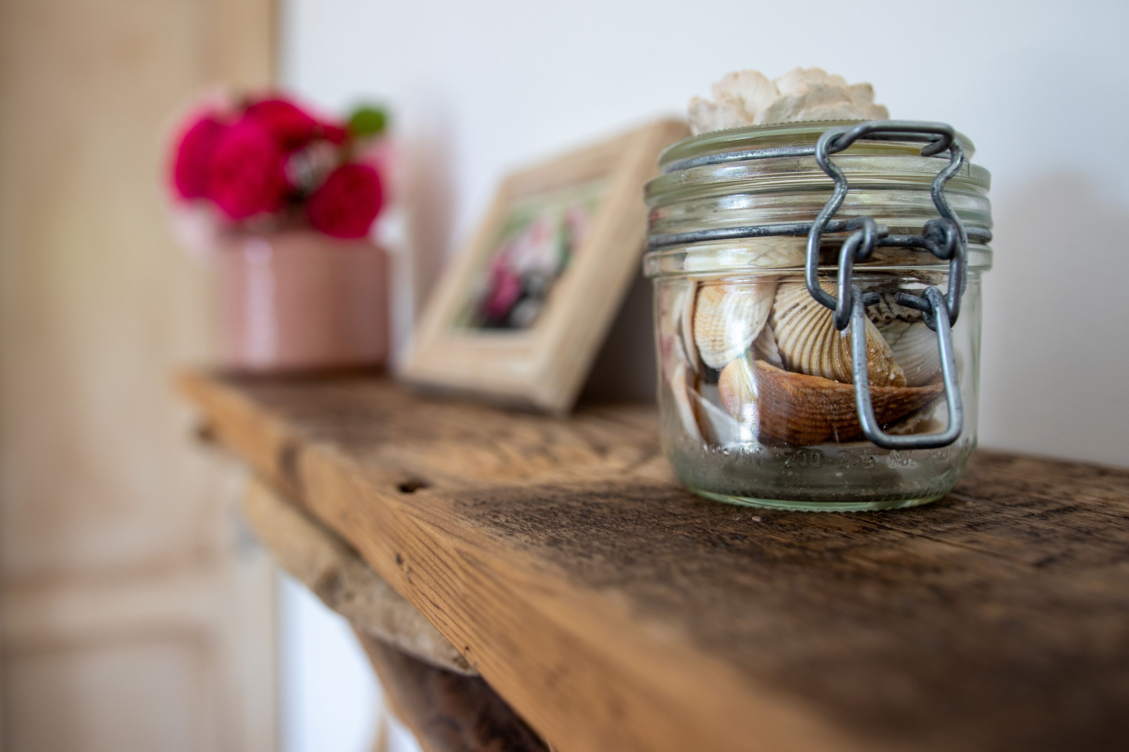 A glass jar with a metal clasp containing seashells, placed on a wooden surface.