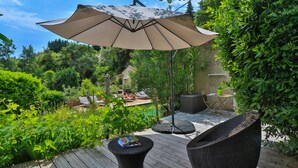 A wooden deck with outdoor furniture, a large umbrella, and lush greenery. - Le Mazet de Tourrettes (Tourrettes-sur-Loup)