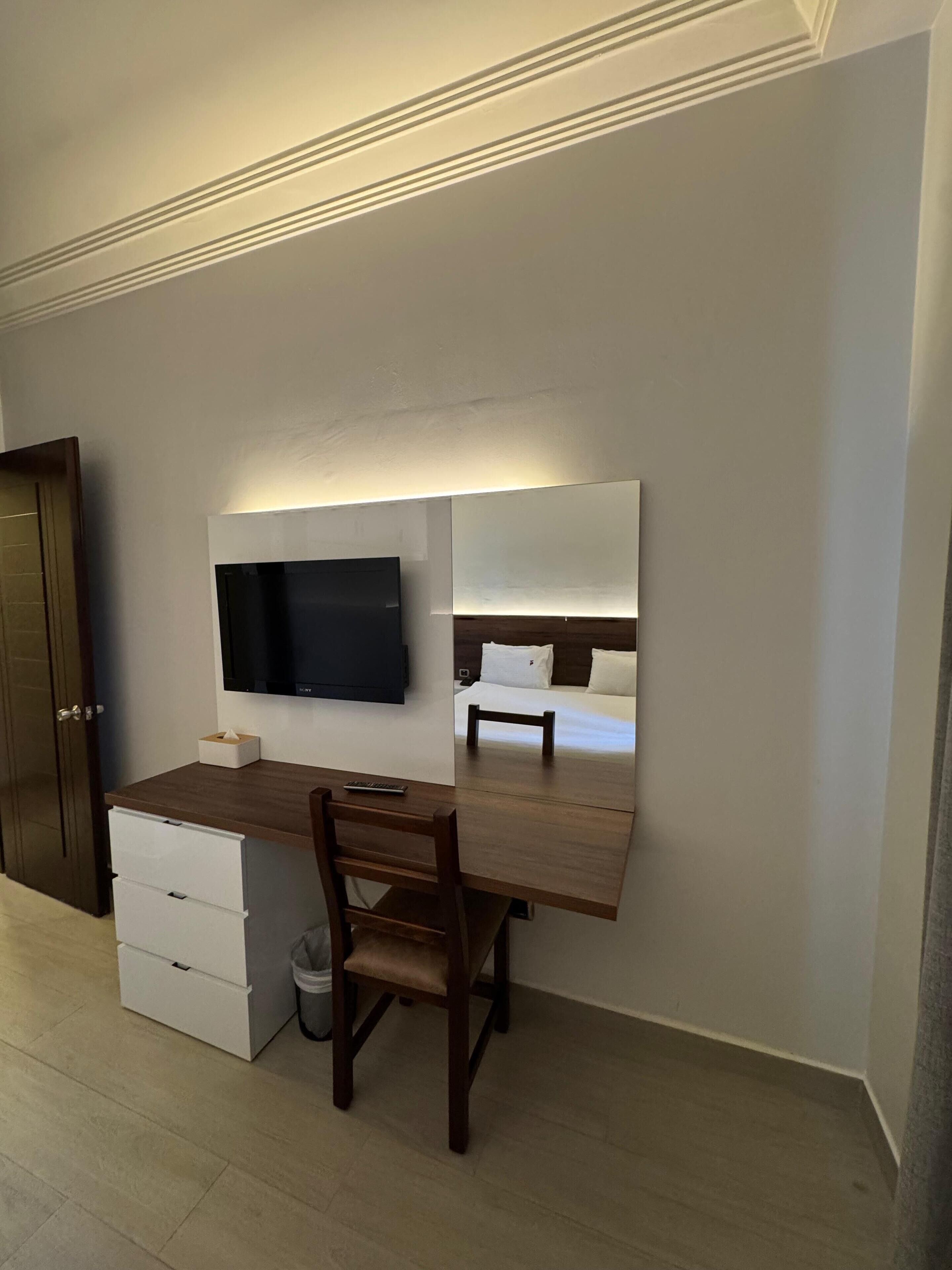 Een hotelkamer met een bureau, stoel, televisie en een bed met hoofdeinde.