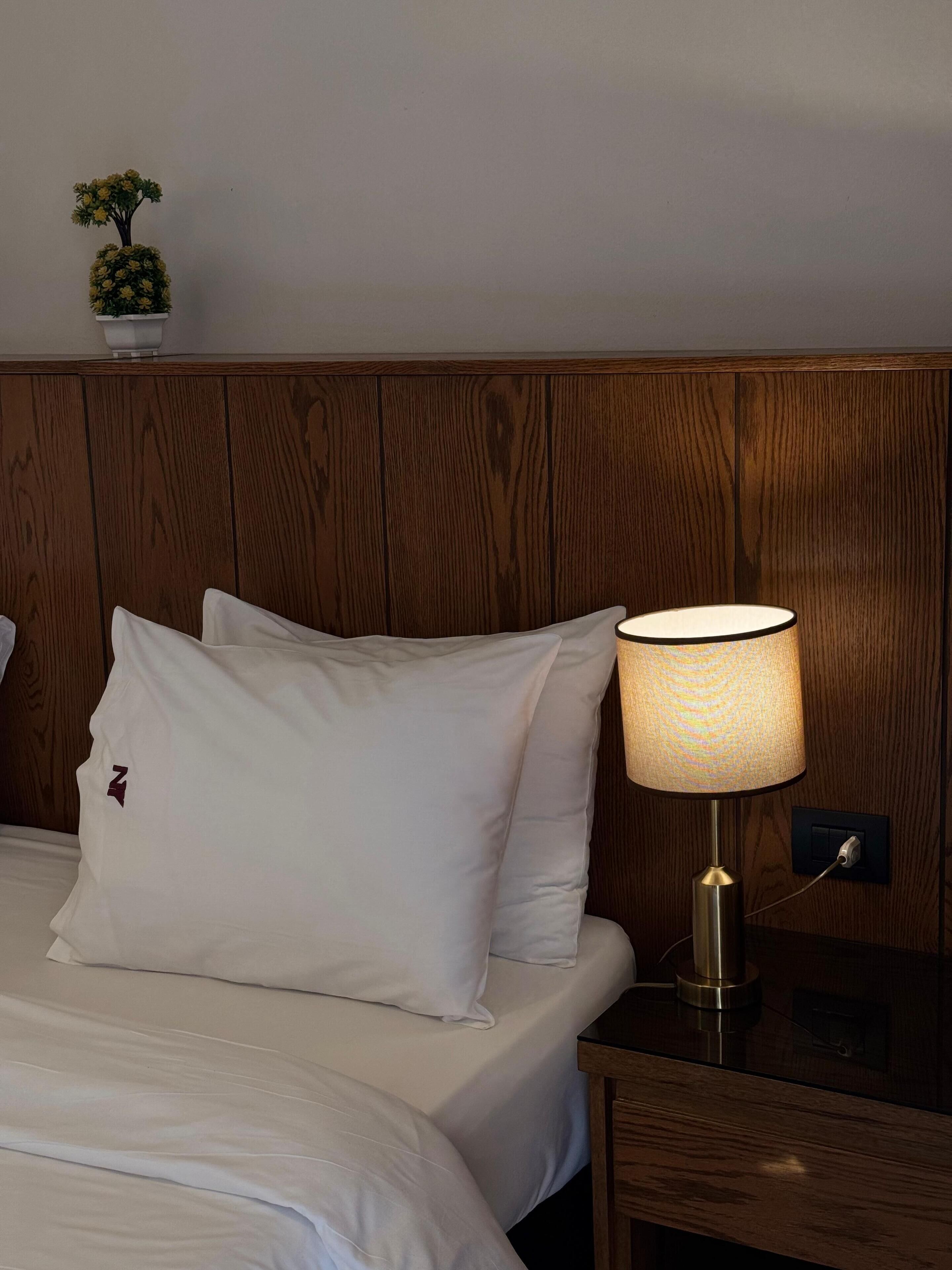 A neatly made bed with white bedding and pillows, a wooden headboard, and a bedside table with a lamp.