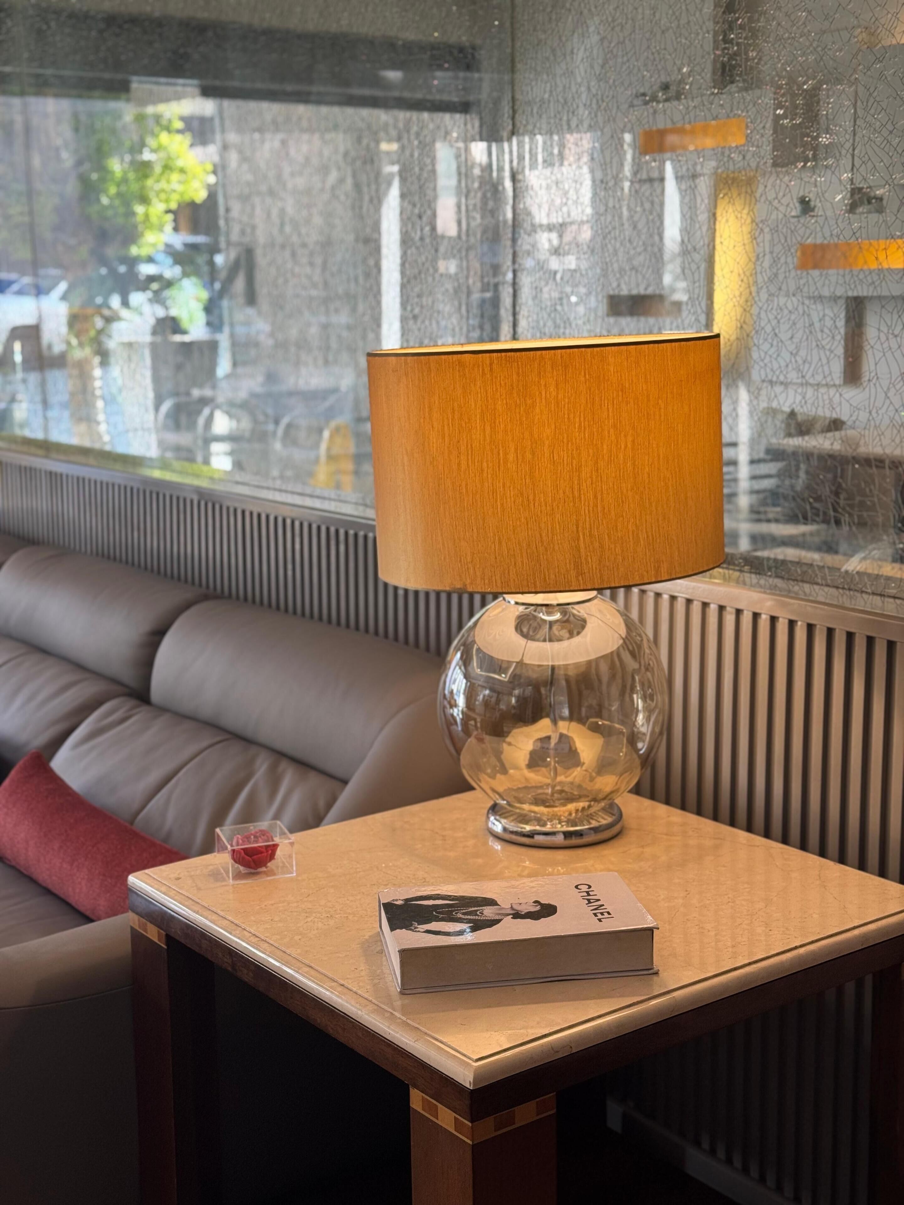 Una sala moderna con un sofá de cuero, una mesa de vidrio transparente, una lámpara con pantalla de madera y un libro.