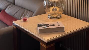 Una sala moderna con un sofá de cuero, una mesa de vidrio transparente, una lámpara con pantalla de madera y un libro.