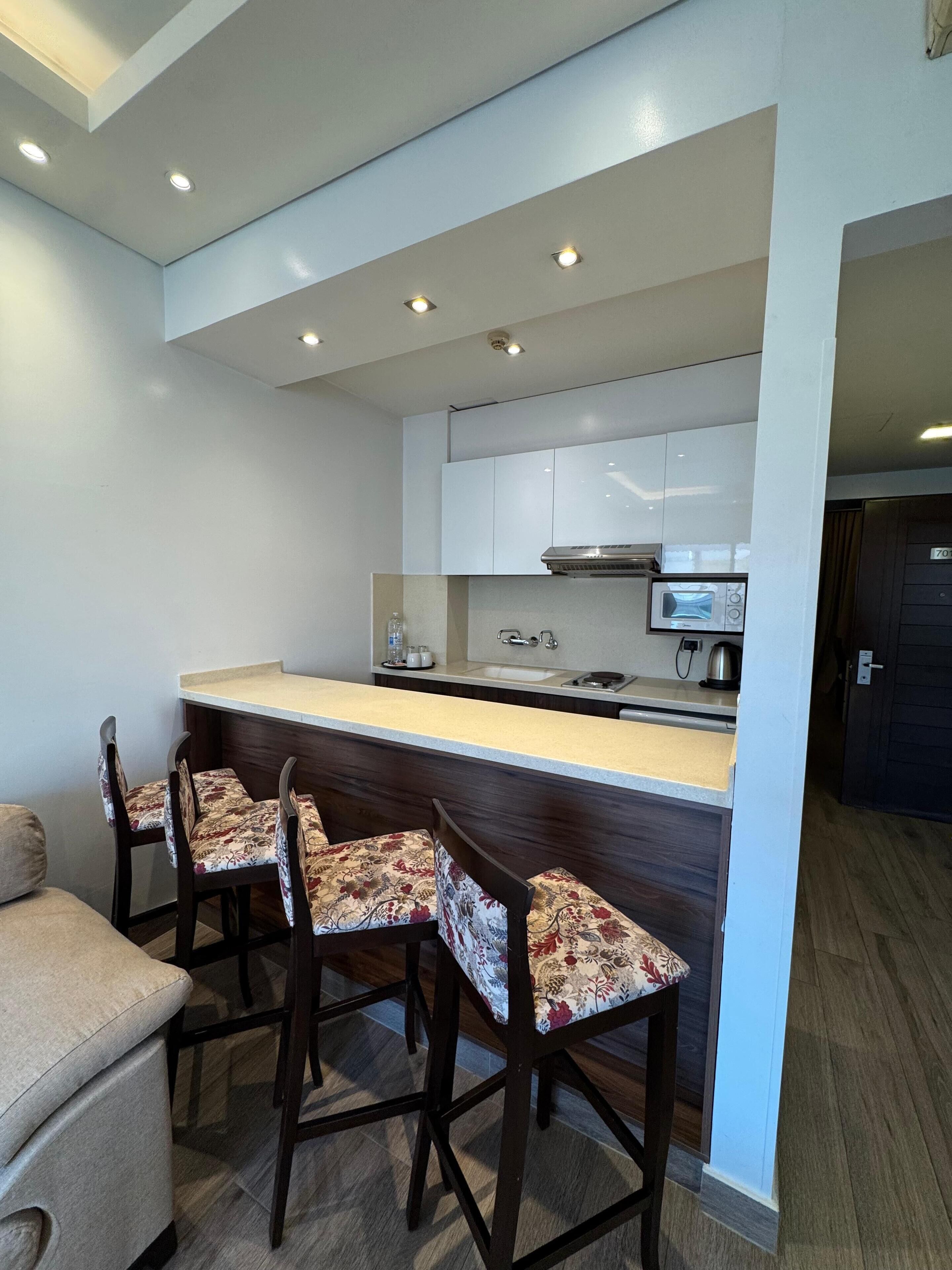 A modern kitchen with white cabinets, a central island, and a microwave. There are four wooden chairs with floral upholstery.