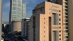 Una calle urbana moderna con edificios altos, incluyendo un prominente rascacielos de vidrio y un edificio color beige con balcones.