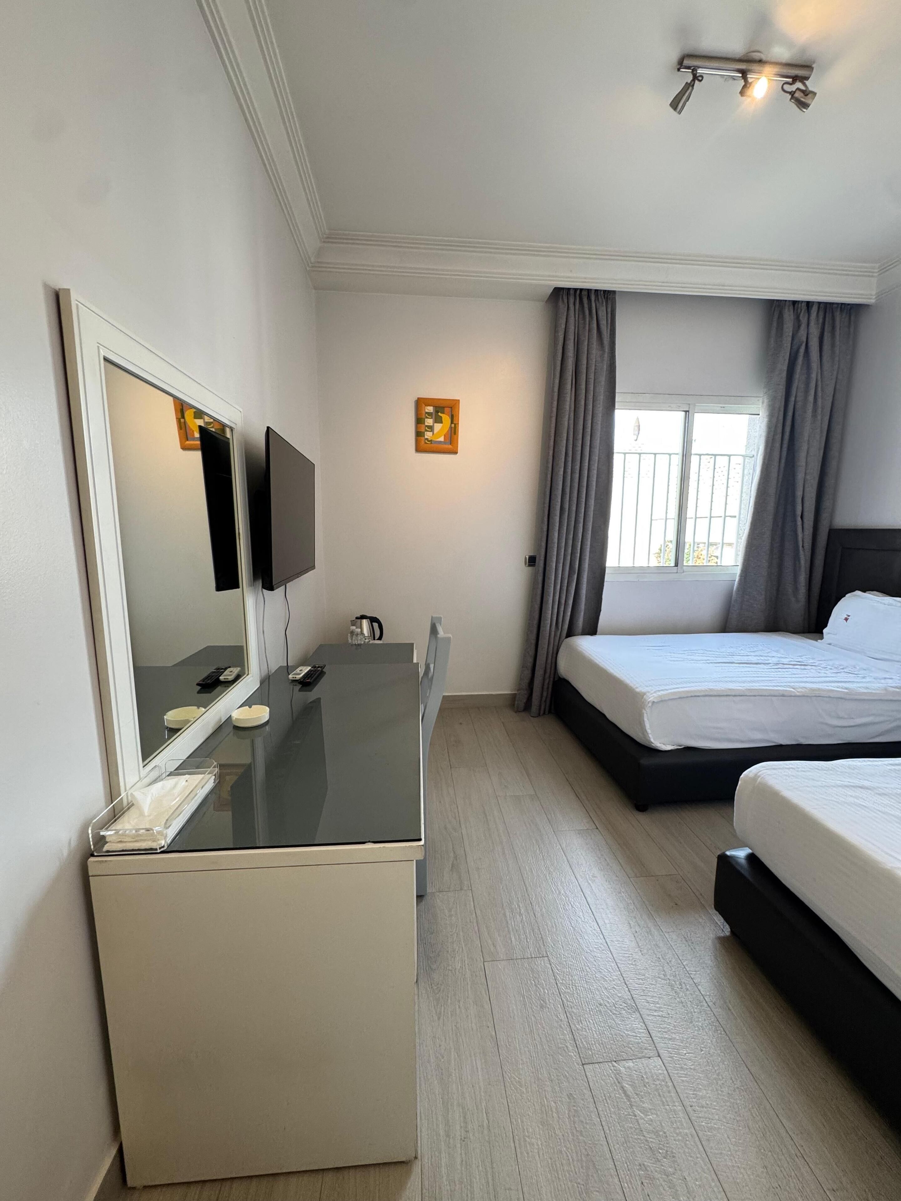 A hotel room with a bed, a desk with a mirror, a television, and a window with curtains.
