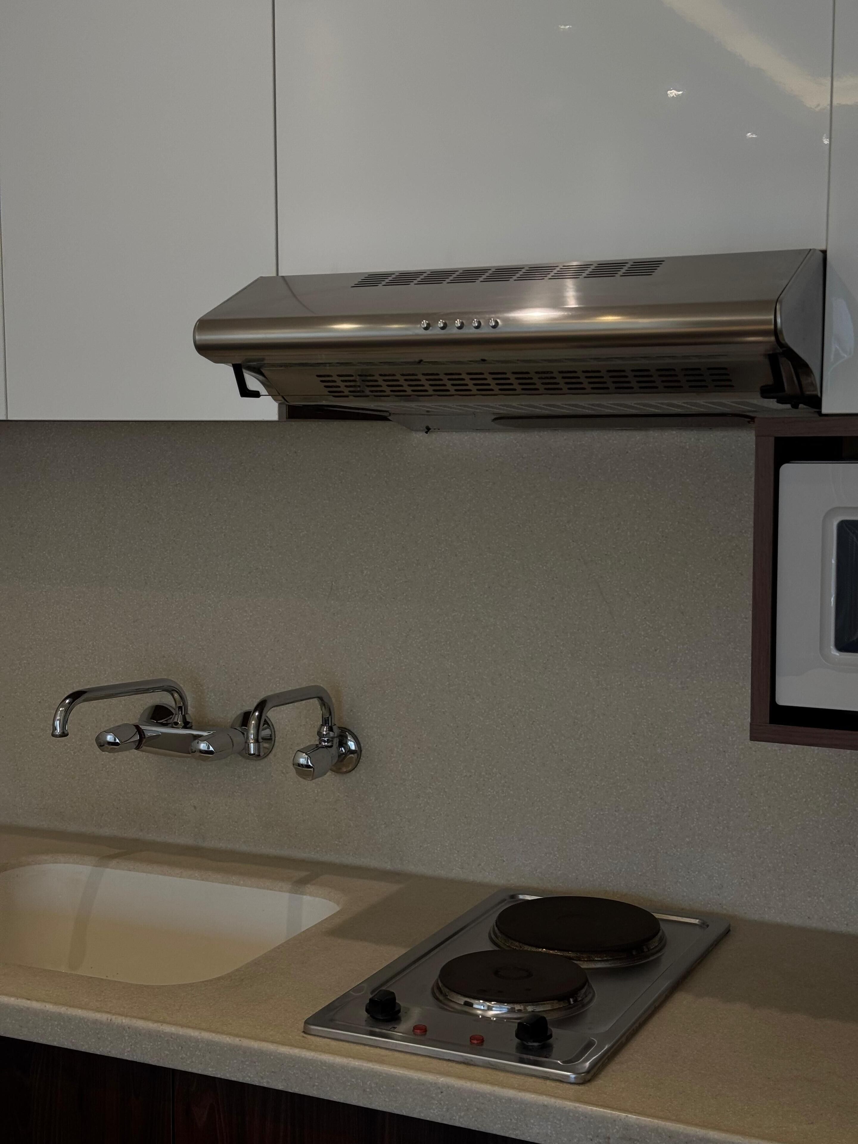 A kitchen with a stainless steel range hood, a double sink with a faucet, and a stovetop with two burners.
