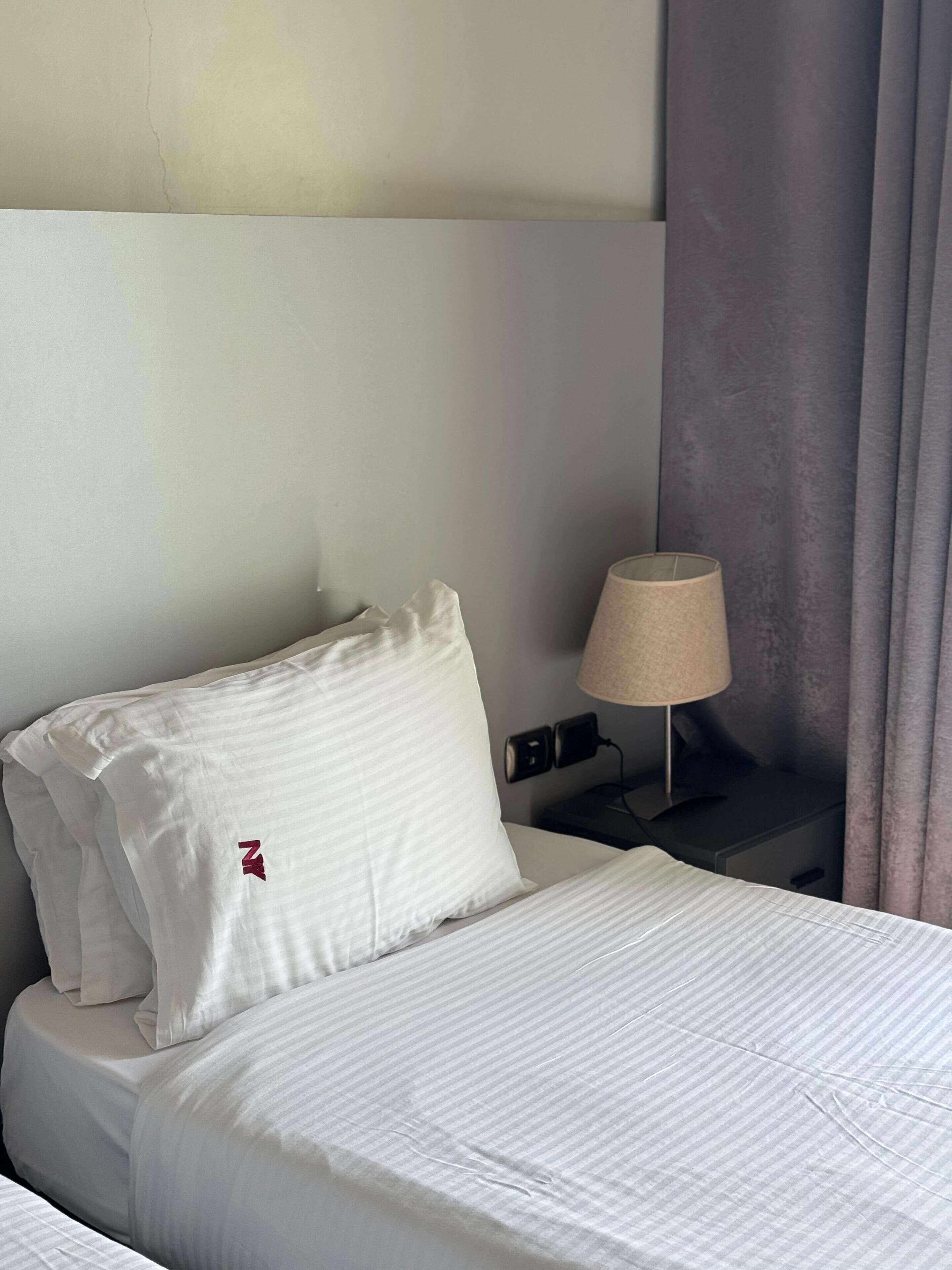 Una habitación de hotel con una cama bien hecha, una lámpara de noche y un enchufe en la pared.