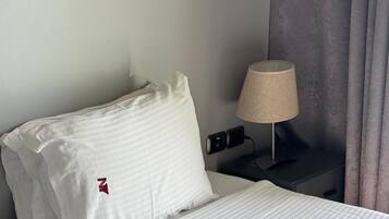 Una habitación de hotel con una cama bien hecha, una lámpara de noche y un enchufe en la pared.