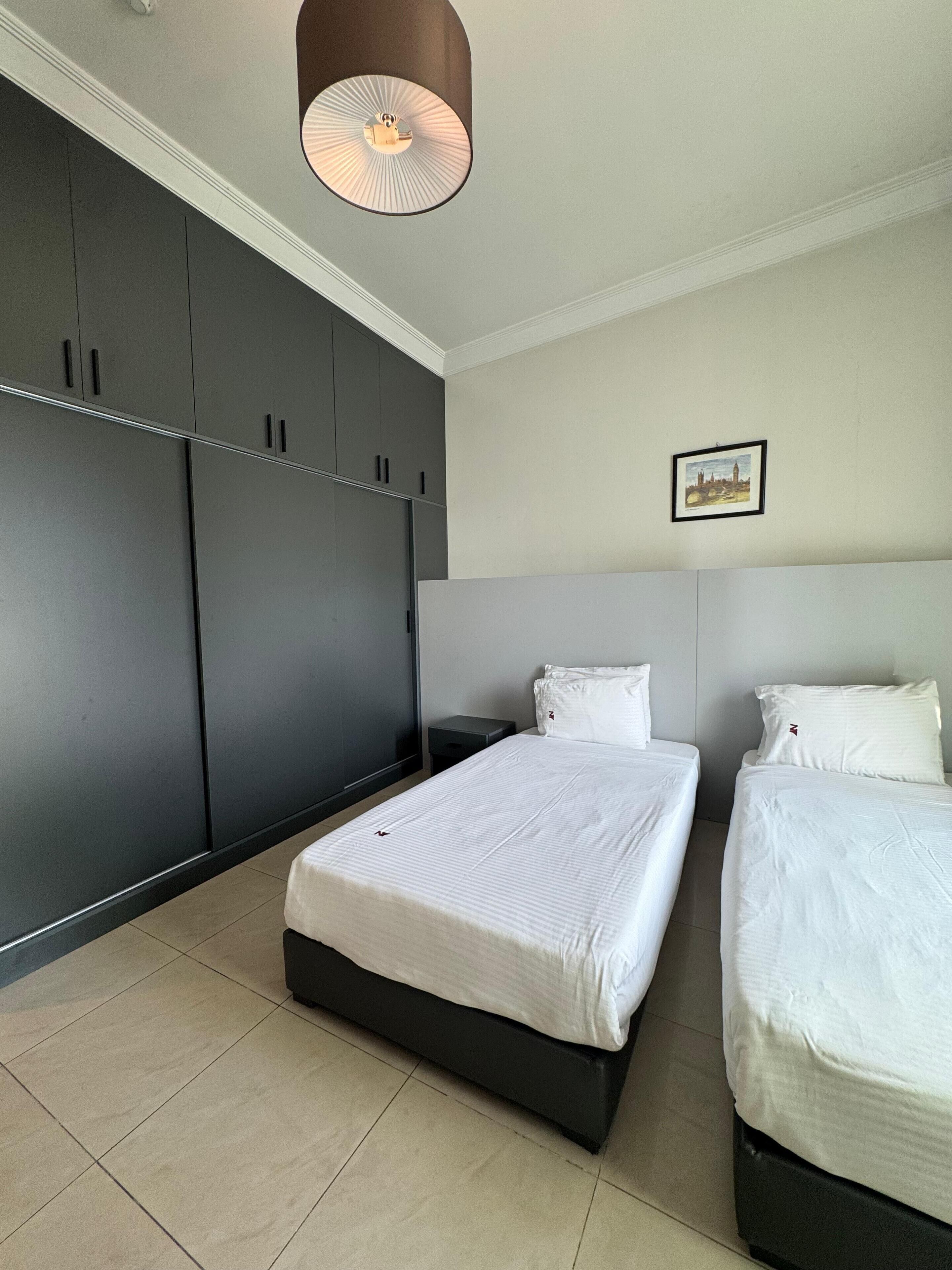 A bedroom with two beds, a large wardrobe, and a ceiling light fixture.