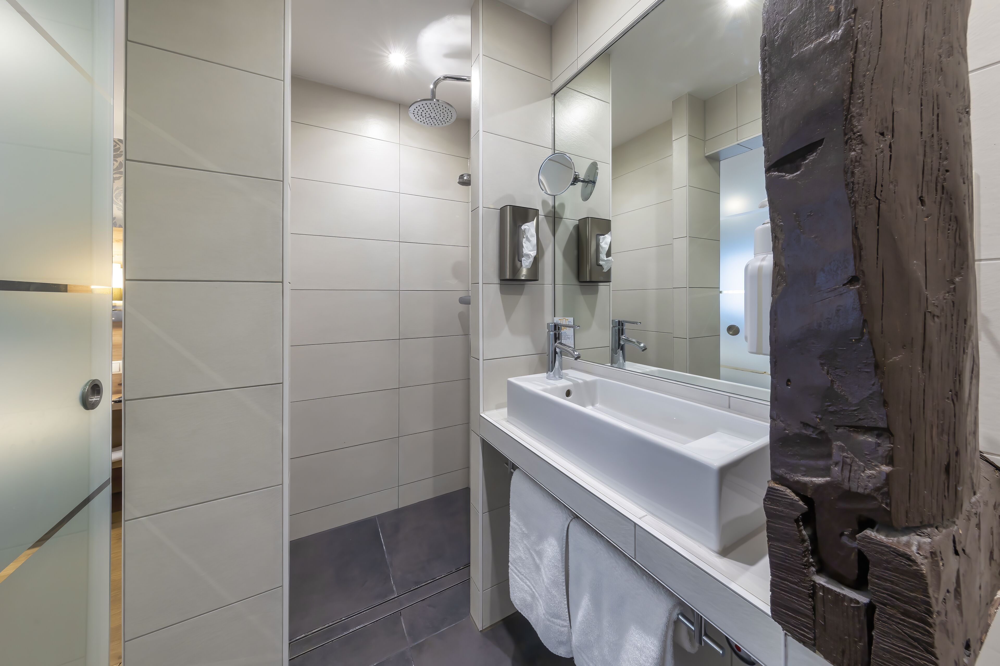Een moderne badkamer met een grote spiegel, een witte wastafel en een douche.