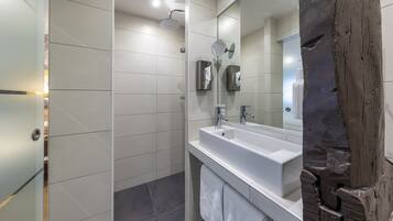 Een moderne badkamer met een grote spiegel, een witte wastafel en een douche.