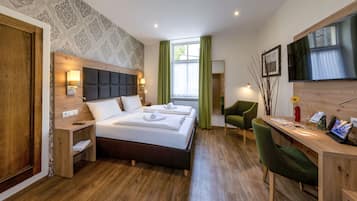A modern hotel room with a large bed, a desk, a chair, and a TV.